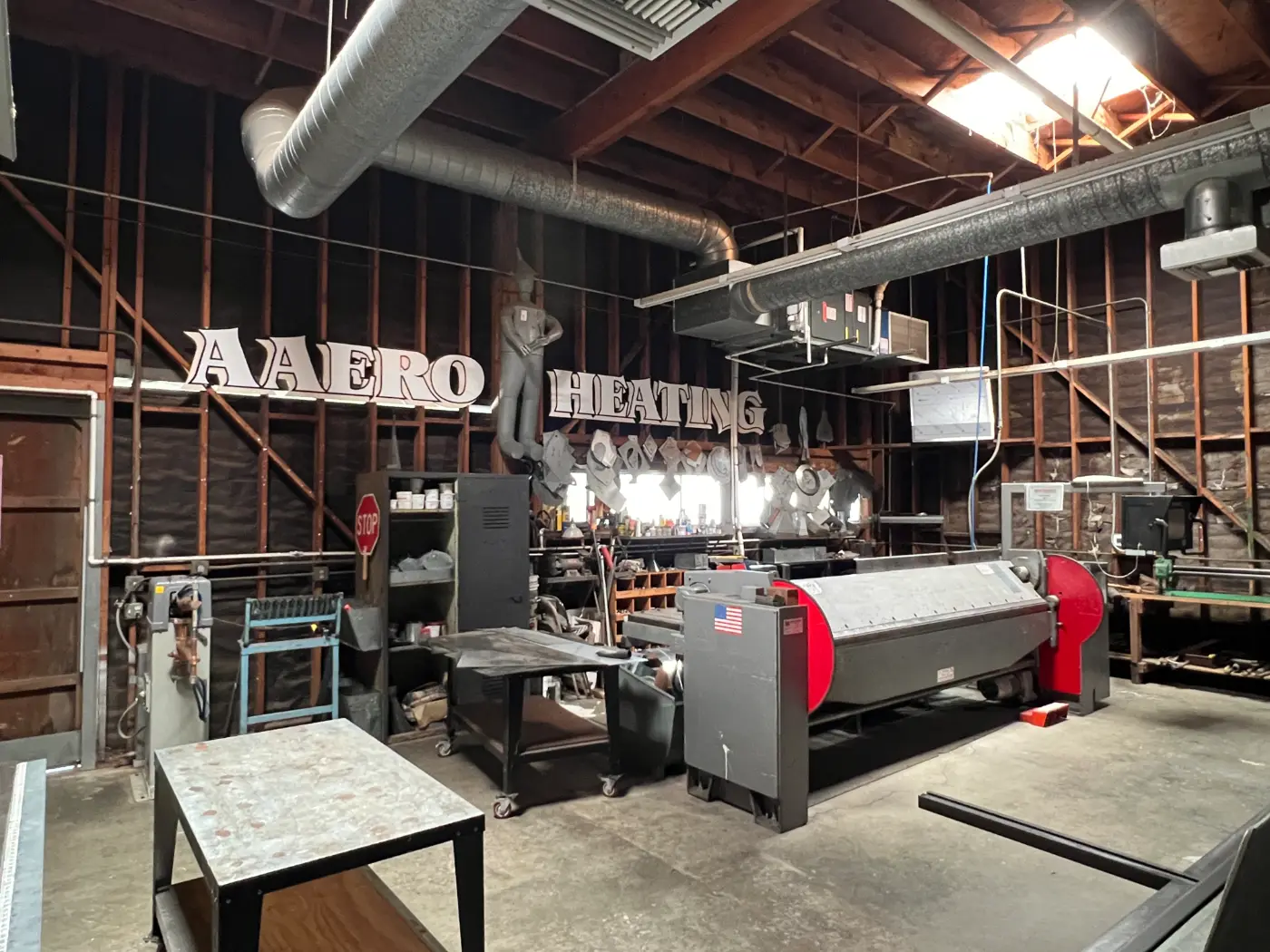 Inside the AAERO HVAC and Sheet Metal fabrication shop in Novato with the custom ductwork brake and forming equipment beneath the original Aaero Heating sign
